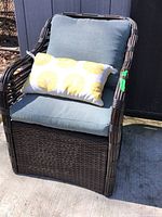 Front view of rattan style patio chair with blue cushions and lemon print pillow