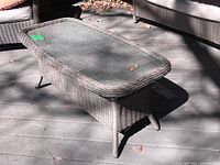 Three-quarter front view showing wicker base and glass top on deck