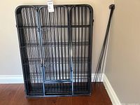 Front view of 8 black metal dog pen panels leaning against wall with door panel visible.