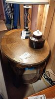 Oval wooden end table with a lamp and ceramic jar on top, showing surface wear and scratches.