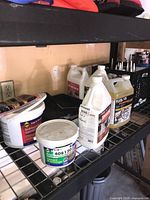 Shelf with containers including Sakrete self-bonding cement bucket, Primus efflorescence cleaner bottles, and Flexlock Eco Seal jug.
