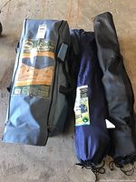 Four fabric carrying bags containing folding armchairs and the portable bed, showing the Escort queen size portable bed label on the gray bag and three other black/navy bags.