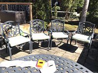 Four metal patio chairs arranged on a stone patio surface