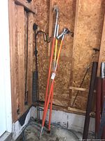 Three orange fiberglass poles leaning against wood-paneled wall