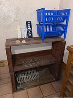 Wooden metal rack with wine bottle holder, three blue stackable plastic bins on top, two thermometers and a wall-mounted bottle opener on the wall above, and two small cards on the rack.