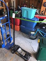 Full view of the Torin Black Jack 3 ton hydraulic floor service jack showing the handle, lifting arm, and wheels in a garage environment.