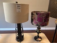 Two table lamps placed side by side on a white table, showing lamp shades and bases.