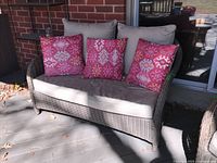 Front view of assembled loveseat with taupe cushions and three pink accent pillows