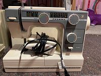 Front view of the beige Janome sewing machine MOD 372 showing stitch pattern dials, width and length controls, foot pedal wrapped with cord.