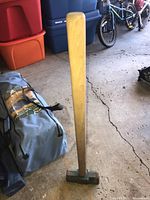 Full view of the sledgehammer showing wooden handle and green metal head on ground in garage.