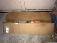 Two rectangular boxes on floor containing the battery minder system components, appearing unopened but box flaps are open.