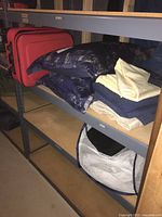 Red suitcase, decorative blue cushions, and assorted folded linens on shelving.