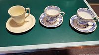 Three teacups with matching saucers: one Bowring ivory white with gold trims, and two Duchess in blue and white patterns with gold trim.