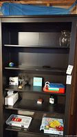 Photo of shelving unit containing items including the glass vase, candle, plastic organizer, puzzles, and other small items
