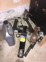 Group photo of six trailer hitches, ball mounts, and a container of antifreeze in a garage corner.