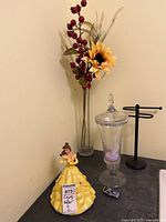 Full view of the lot showing the vase with faux flowers, Disney Belle coin bank, glass jar, metal rack and toy car on a surface.