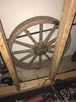 Full view of wooden wagon wheel leaning against a wall and wooden frame structure.