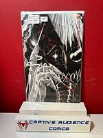 Photo of Batman #1 comic book with black and white minimalist close-up cover art propped on a white stand labeled Captive Audience Comics against red background.