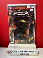 Front cover image of Batman and Robin #1 comic book with lenticular cover showing the dark, atmospheric artwork with Batman holding an umbrella. The comic is sealed and the image includes a display block with Captive Audience Comics branding.