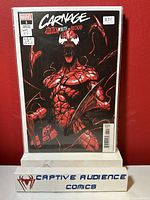 Carnage #1 comic book with black, white, and red cover featuring Carnage character, sealed in a protective plastic sleeve and displayed on a Captive Audience Comics stand.