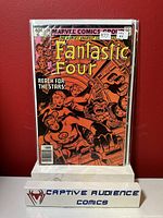 Front cover of Fantastic Four #220 comic book in plastic sleeve against red background, displayed on a white stand labeled Captive Audience Comics.