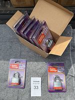 Box with eight sealed Public Storage 1.5" steel laminated padlocks visible, packaged on purple backing cards.
