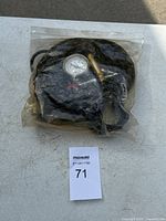 Alternate top-angle view of A/C hoses and pressure gauge sealed in plastic.