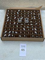 Top view of box showing 100 small white and black salt and pepper shakers in compartmentalized cardboard holder.