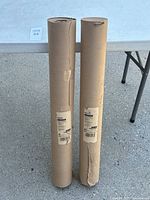 Two vertical rolls of brown builder's or painter's paper standing upright on a concrete surface beside a table.