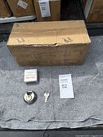 Closed cardboard box likely containing the case of disc locks with one lock, key, and tag labeled 'Item #634' displayed in front of the box.