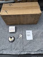 Overview of cardboard box, one padlock, small box, two keys and lot tag