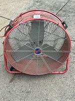 Front view showing the red metal body, steel wire grille, and central fan blades with logo.