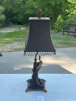 Full view of the lamp with black lampshade and peacock base taken outdoors