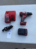 Photo showing the drill, charger, and battery placed on a white table surface.