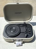 Front view of an open suitcase-style Crosley record player showing turntable, tonearm, and controls inside.