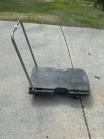 Rolling cart set up low on the ground showing black plastic base platform and metal handle upright.