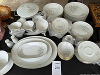 Photo showing most of the porcelain dinnerware laid out including plates, bowls, cups, saucers, and serving platters with bubble wrap and surrounded by other items.