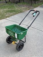 Angle view of the green Scotts spreader standing on a concrete driveway with grass in the background.