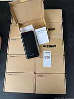 Ten cardboard boxes each labeled 'POWER BANK', one box open showing black and red power bank with user manual and protective sleeve.