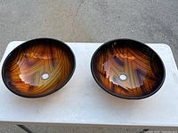 Two round amber glass sinks set on a white table outdoors, showing their polished exterior and bowl shapes.