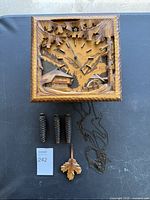 Top view of the vintage Kuner cuckoo clock with weights, pendulum and chain laid out below. Shows entire clock face and carved details.