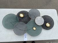 Set of eight decorative circular metal wall art plates arranged on a white table, showing different sizes and colors with three pieces having gold bowl accents.