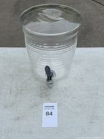 Clear plastic water dispenser with a lid and front spigot, placed on a white surface outdoors.