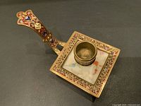 Top view of the square bronze candle holder with champleve enamel around the base and on the handle, showing the marble inset with floral painting.