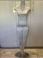 Front view of tall white modernist female figure sculpture on round metal base against white cabinetry.