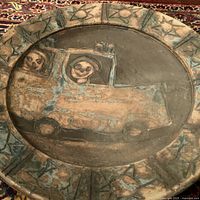 Top view of large pottery charger showing painted figures in vehicle with border decoration.