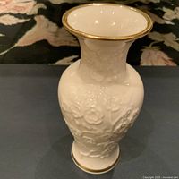 Front angle view of Lenox cream porcelain vase showing embossed floral patterns and gold trim on rim and base.