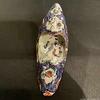 Top view of the shoe-shaped enamel dish showing painted bird inside and floral decorations on the toe and heel areas against a dark background.