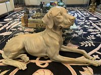 Front and side view of large seated dog sculpture on patterned carpet with glass table and other decor in background.