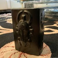 Photo of vintage black ceramic vase showing embossed African tribal mask design on front and texture on sides.